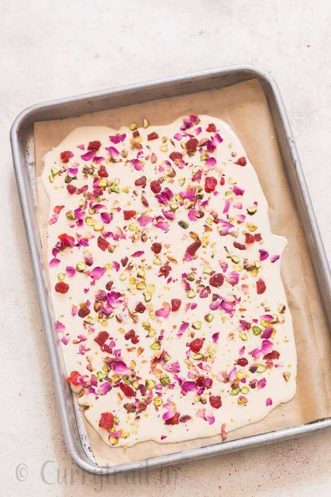 white chocolate bark with dried rose petals, pistachios and dried strawberries on a baking sheet