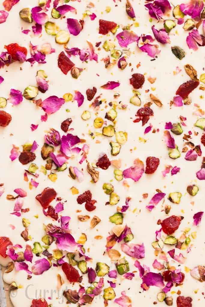 white chocolate bark with dried rose petals, pistachios and dried strawberries on a baking sheet