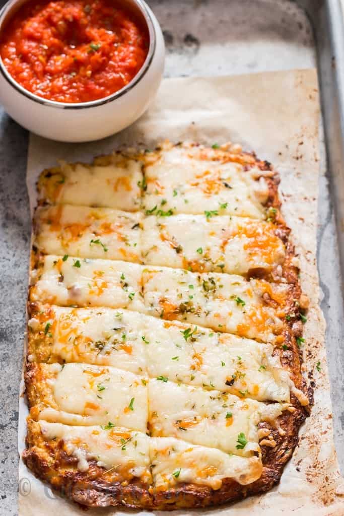 cheesy cauliflower breadsticks on baking tray served with spicy marinara sauce