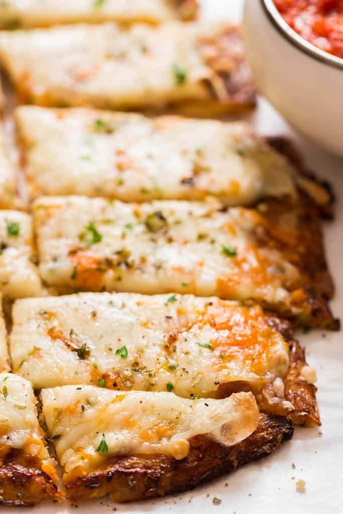 close up of cheesy low carb breadsticks on baking tray served with spicy marinara sauce