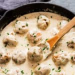 creamy white sauce with chicken meatballs cooked in it in cast iron skillet with text