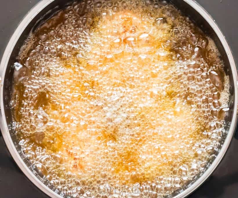 Deep frying chicken in hot oil in a shallow pan.