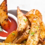 Close-up view of baked potato wedges on a plate with ketchup on the side with text overlay.