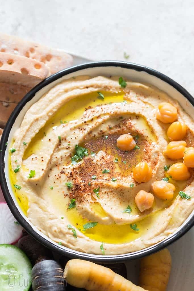hummus recipe served in white bowl with veggies and breadstick on side