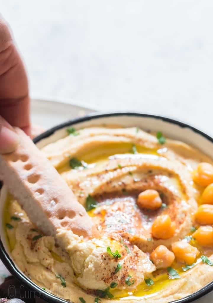 bread scooping out homemade chickpea dip from white bowl