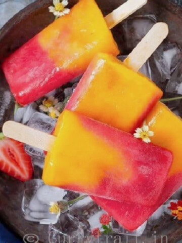 strawberry and mango popsicles in a tray with ice cubes.
