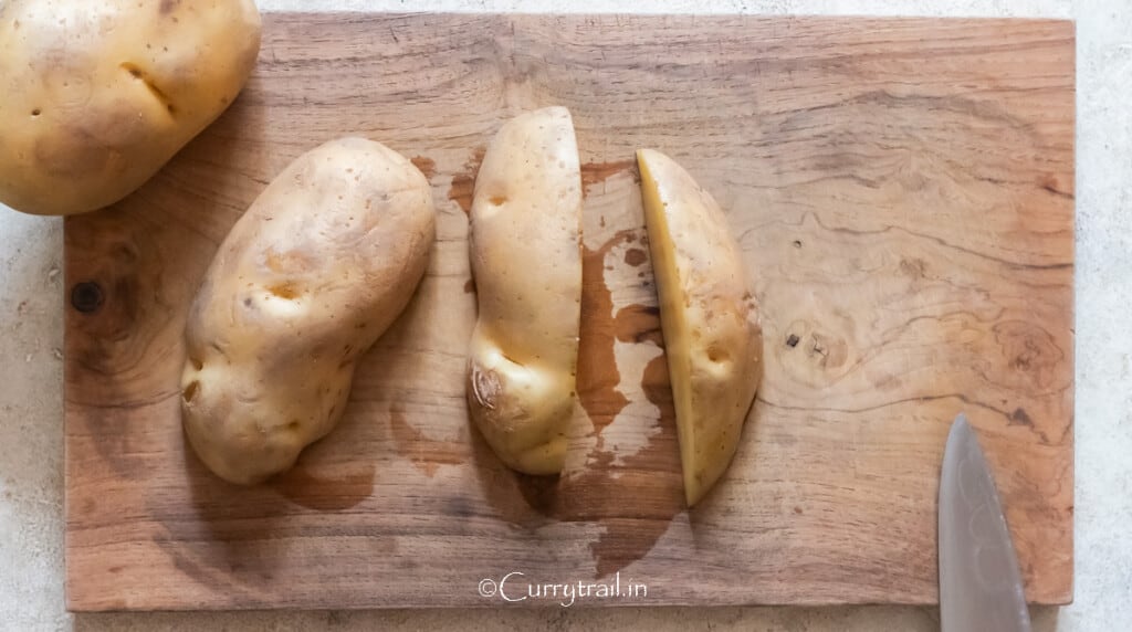 cutting the potato on a wooden board to cut it into half to cut wedges.