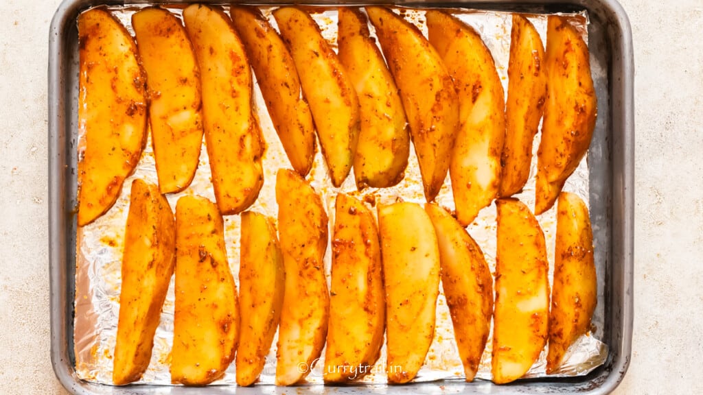 potato wedges seasoned with spices arranged in one layer on a baking tray lined with aluminum foil.