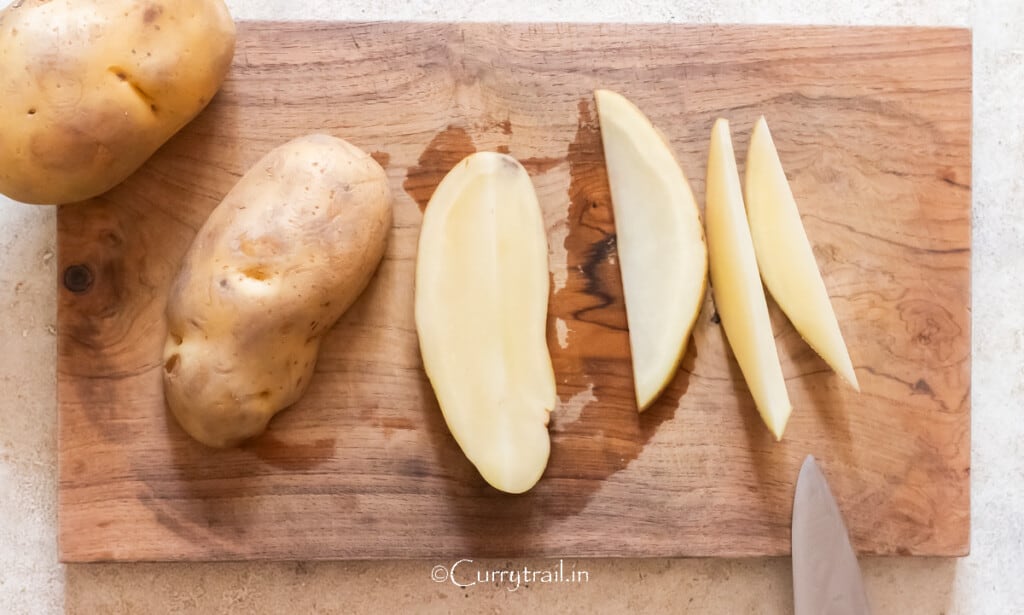cutting the potato on a wooden board to cut it into half to cut wedges.