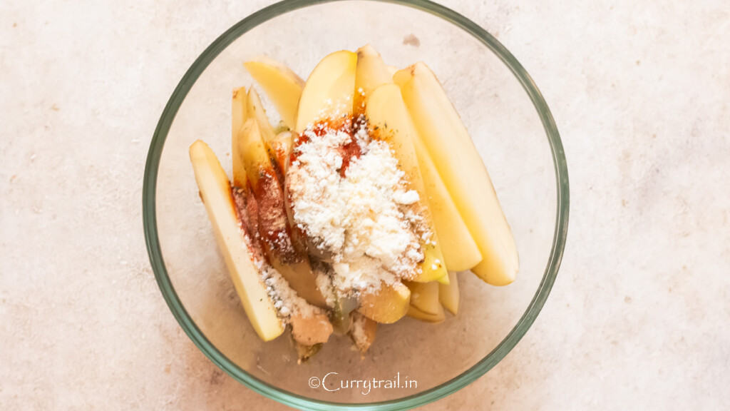 potato wedges in a bowl with seasoning spices and parmesan cheese powder.