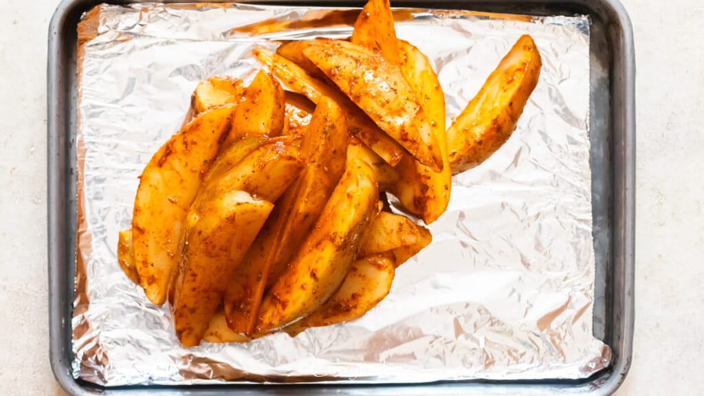 seasoned potato wedges on a baking tray lined with aluminum foil.