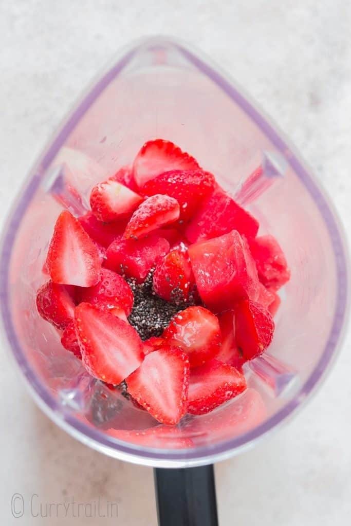 all ingredients to make a smoothie with watermelon and frozen strawberries added to a blender.