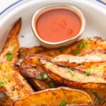 Close-up view of baked potato wedges on a plate with ketchup on the side.