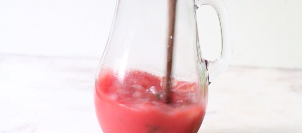 stirring watermelon mojito in a pitcher.