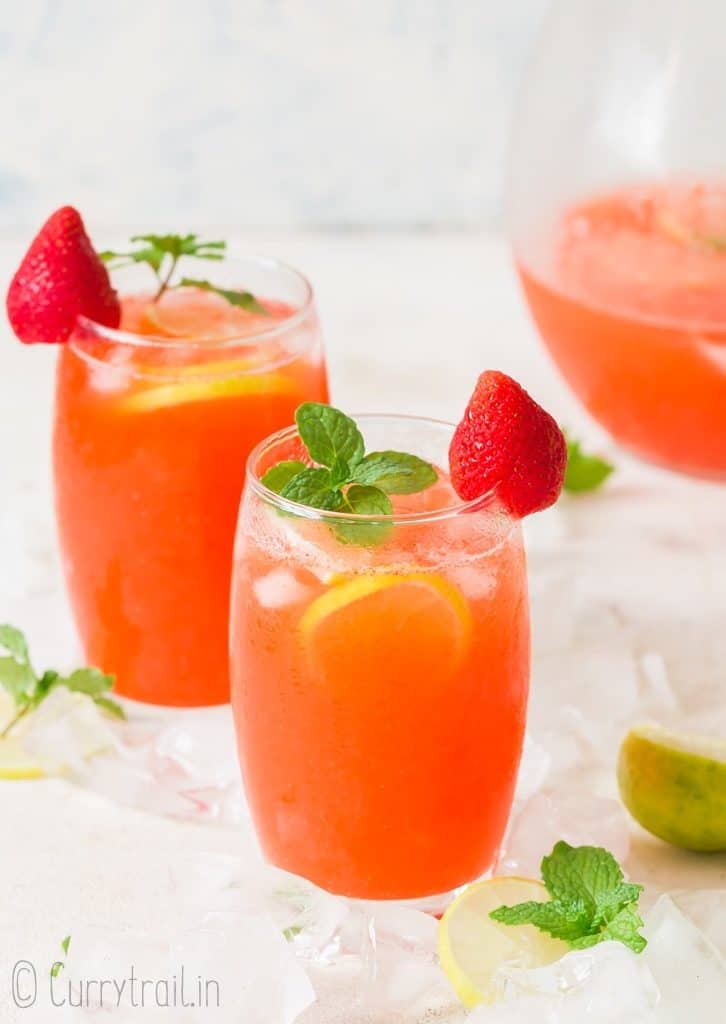 fresh strawberry lemonade served in two glasses with a pitcher on the side