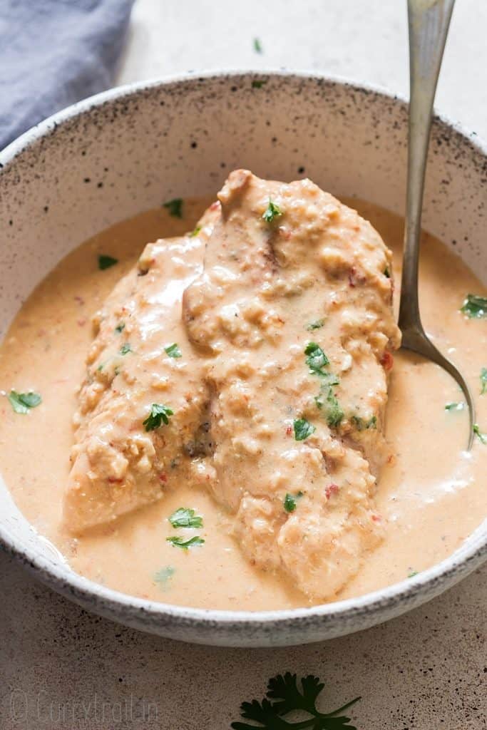 two chicken breasts in creamy chipotle chicken recipe in white bowl with a spoon