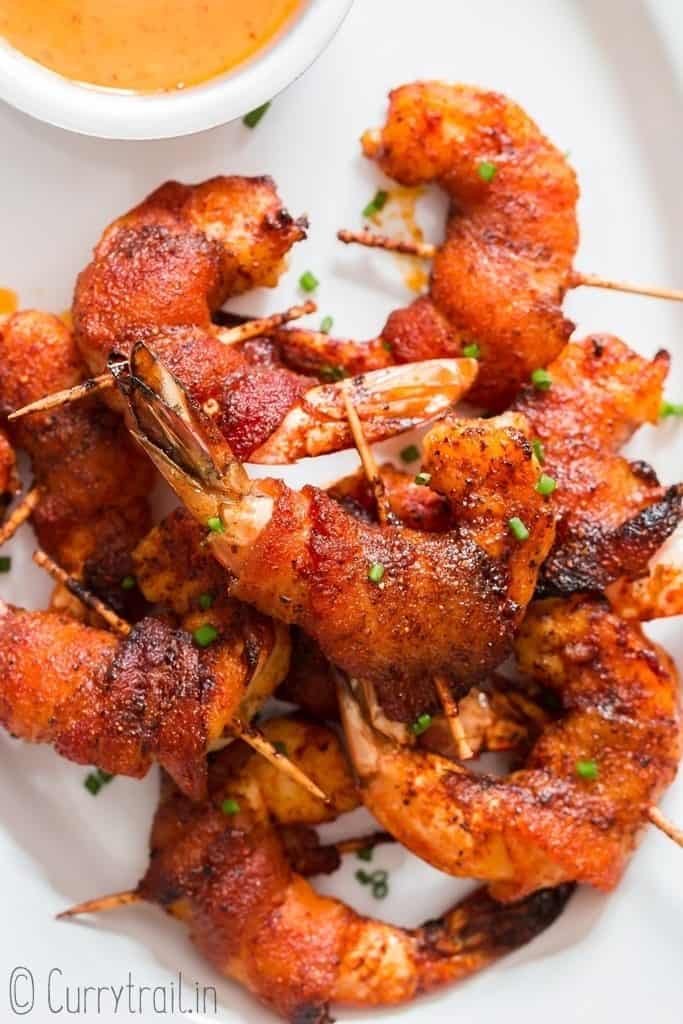 grilled bacon wrapped shrimp on white oval plate with spicy dipping sauce on side
