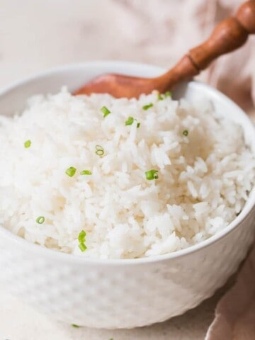 steamed rice with chives on top in white bowl with wooden spoon