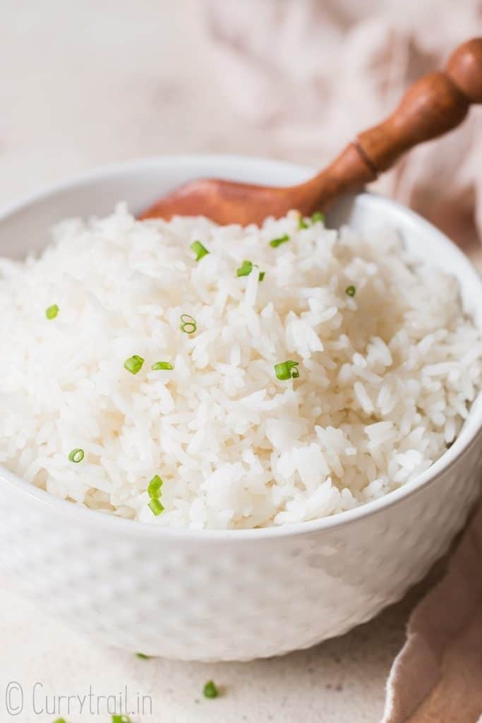 steamed rice with chives on top in white bowl with wooden spoon