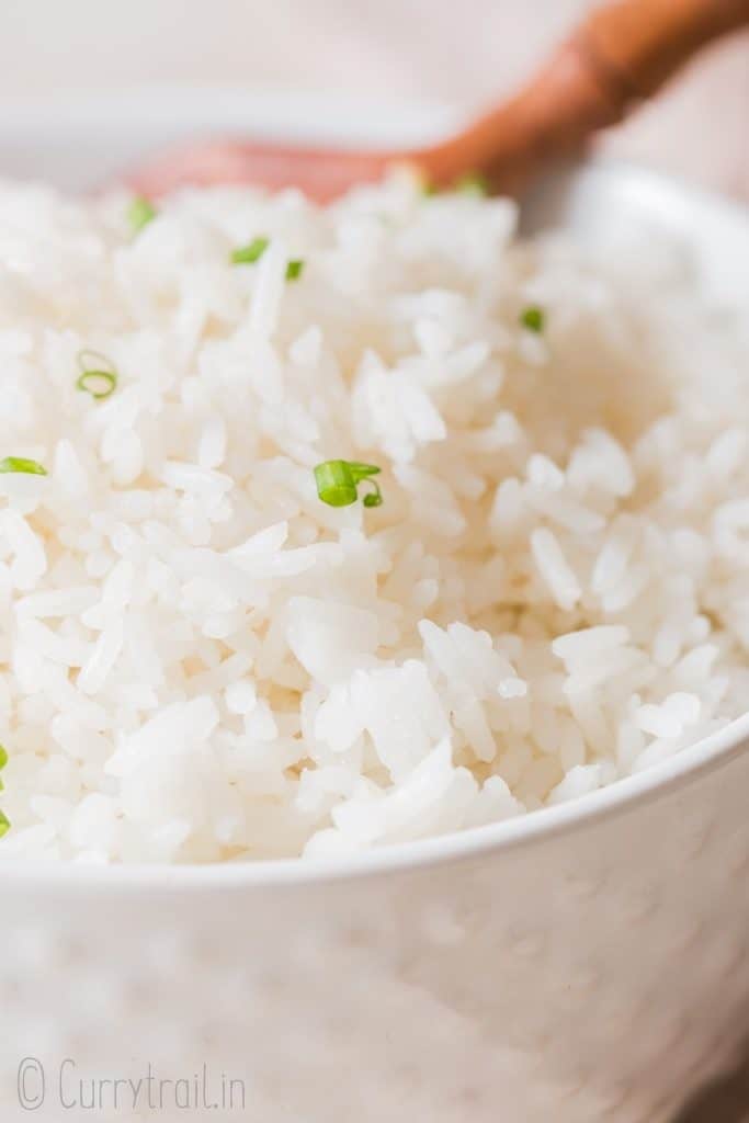 close up view of steamed rice with chives on top in white bowl