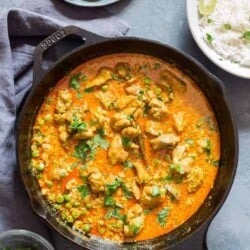 chicken curry in cast iron pan with rice and cucumbers placed on the sides