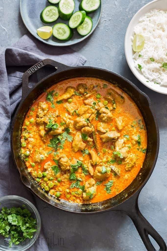 chicken curry in cast iron pan with rice and cucumbers placed on the sides