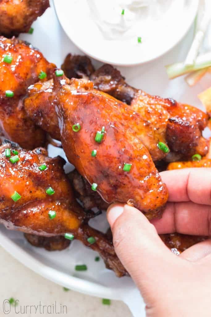 juicy instant pot chicken wings on white plate with a piece held in hand