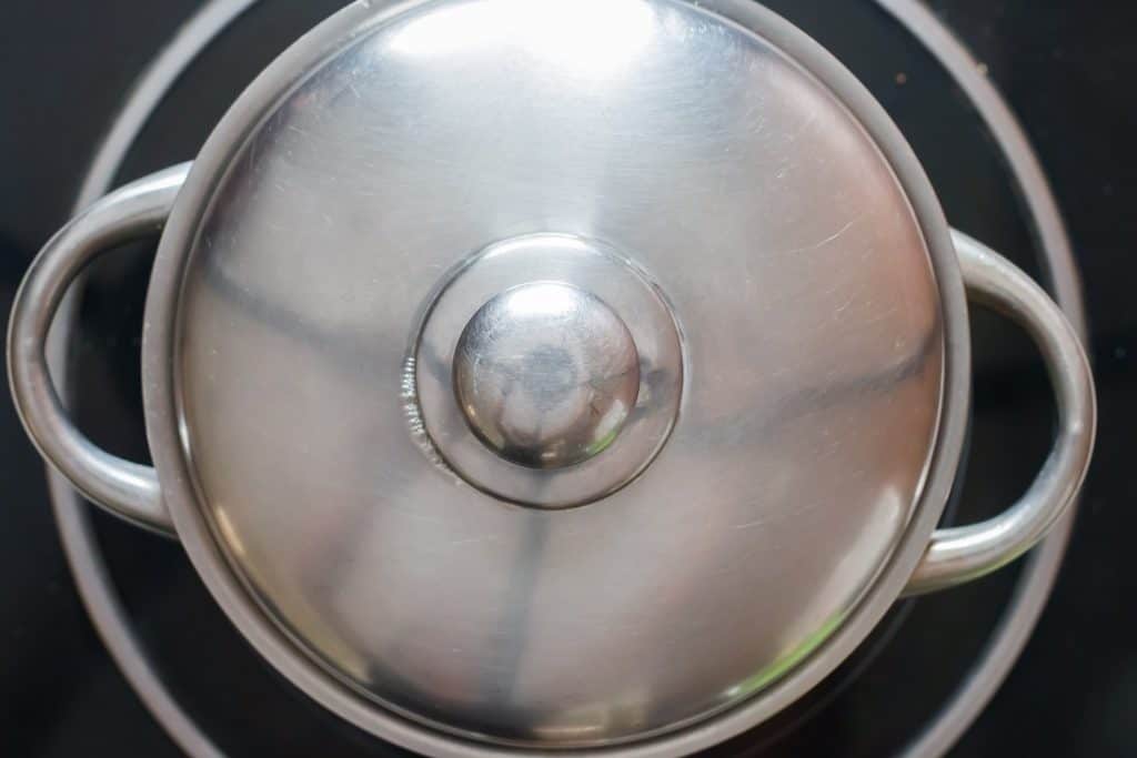 pot covered with a lid with rice and water cooking in it.