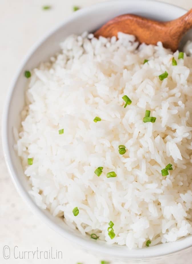 steamed rice with chives on top in white bowl with wooden spoon