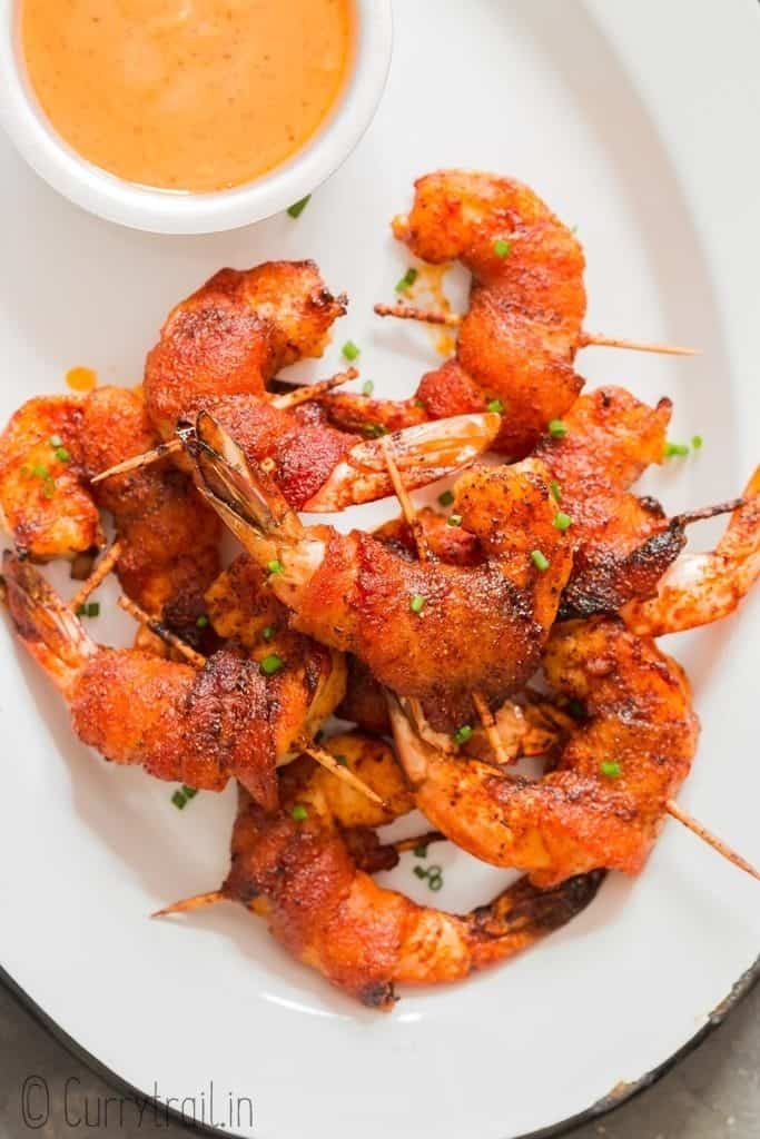 spicy sweet bacon wrapped shrimp on white plate with spicy dipping sauce