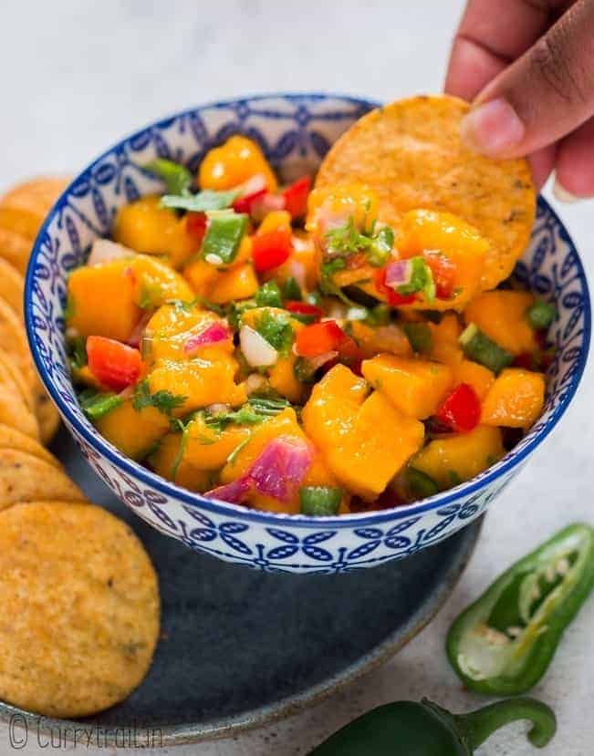 scooping mango salsa with nachos from blue ceramic bowl