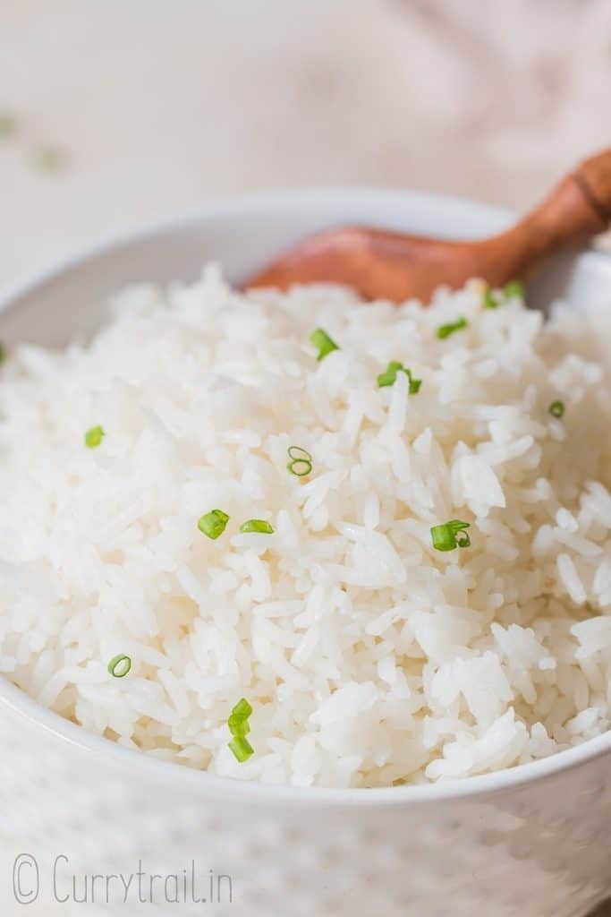 steamed rice with chives on top in white bowl with wooden spoon