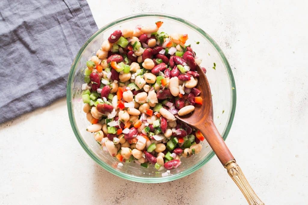3 bean salad tossed in glass bowl with wooden spoon