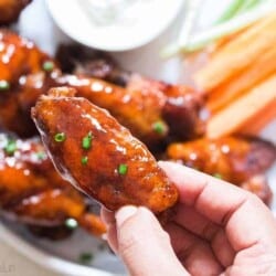 juicy instant pot chicken wings on white plate with a piece held in hand
