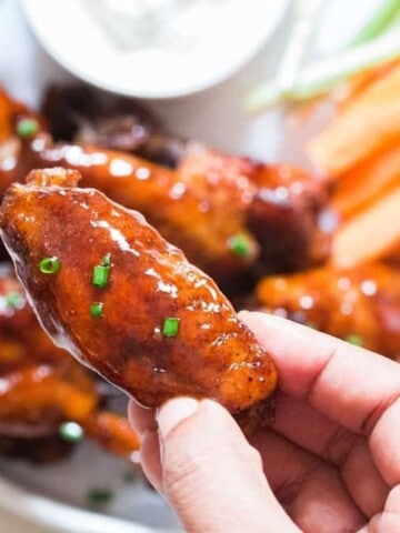 juicy instant pot chicken wings on white plate with a piece held in hand