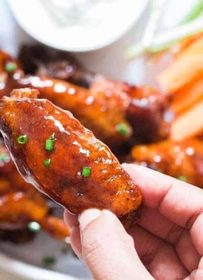 juicy instant pot chicken wings on white plate with a piece held in hand