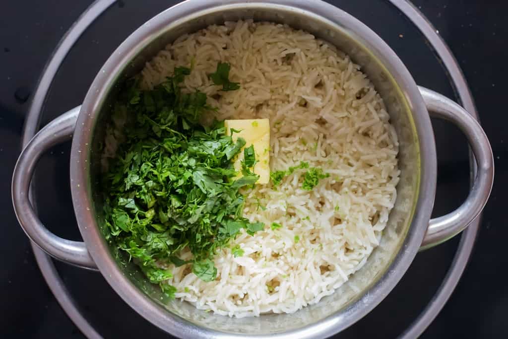 fresh cilantro and butter are added to cooked rice in a pan.