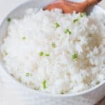 steamed rice with chives on top in white bowl with wooden spoon