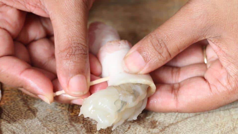 securing bacon wrap around shrimp using a toothpick.