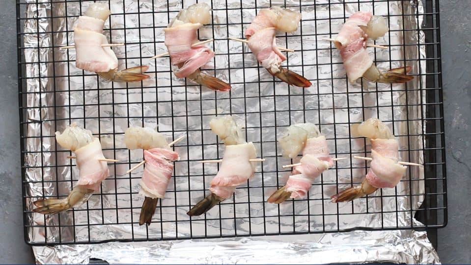 shrimp wrapped in bacon placed on a wire rack lined over a baking tray.