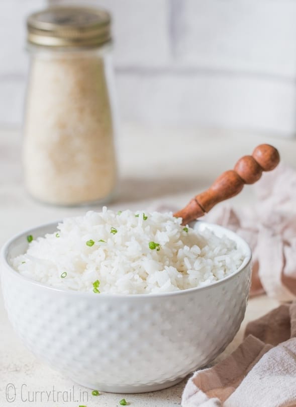 tender steamed rice in white bowl with a jar of rice in the background