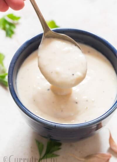 pouring luscious garlic Parmesan sauce from a spoon in blue bowl