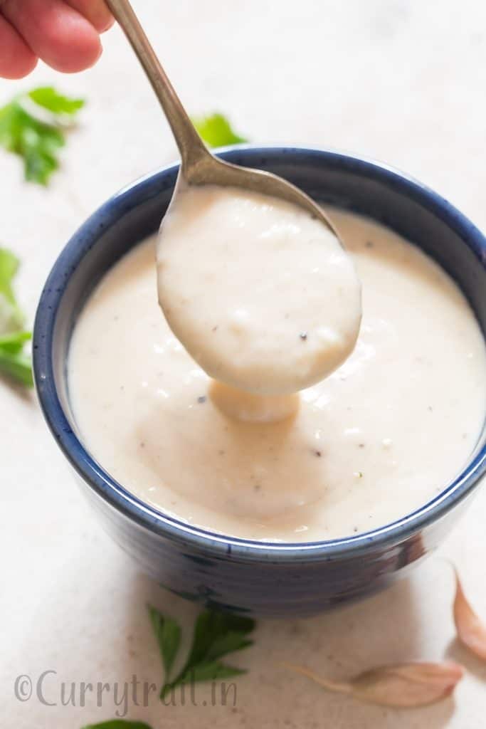 pouring luscious garlic Parmesan sauce from a spoon in blue bowl