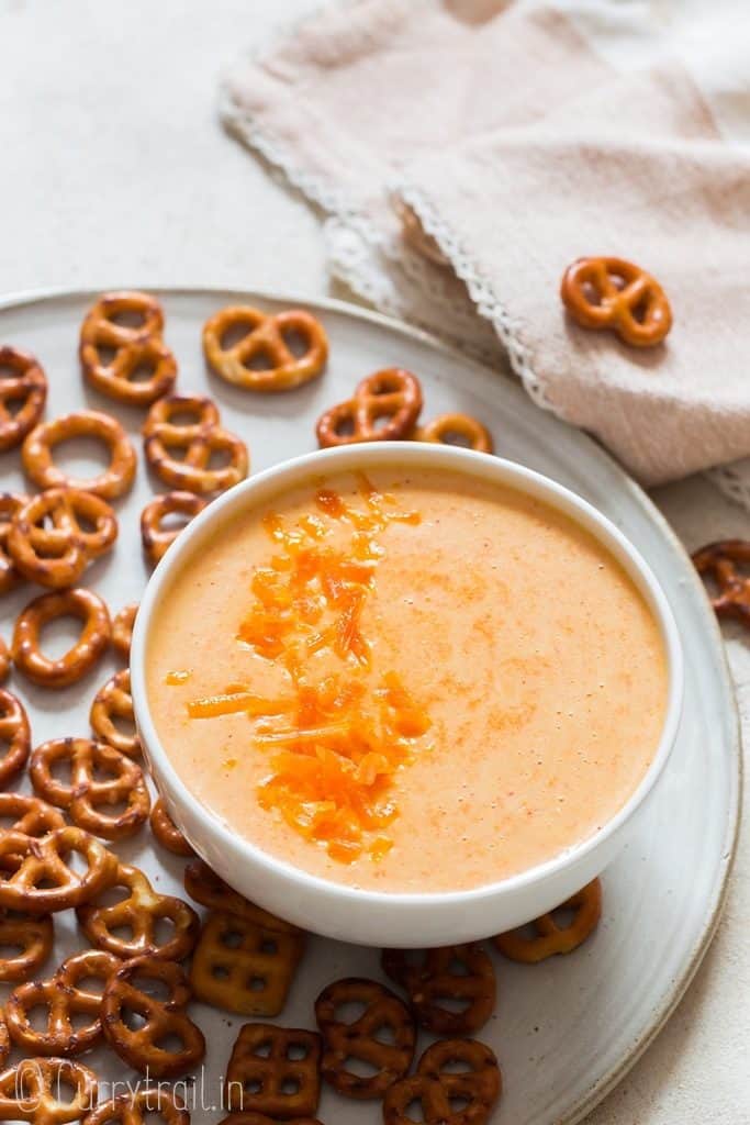 beer cheese dip served in white bowl with pretzels on side