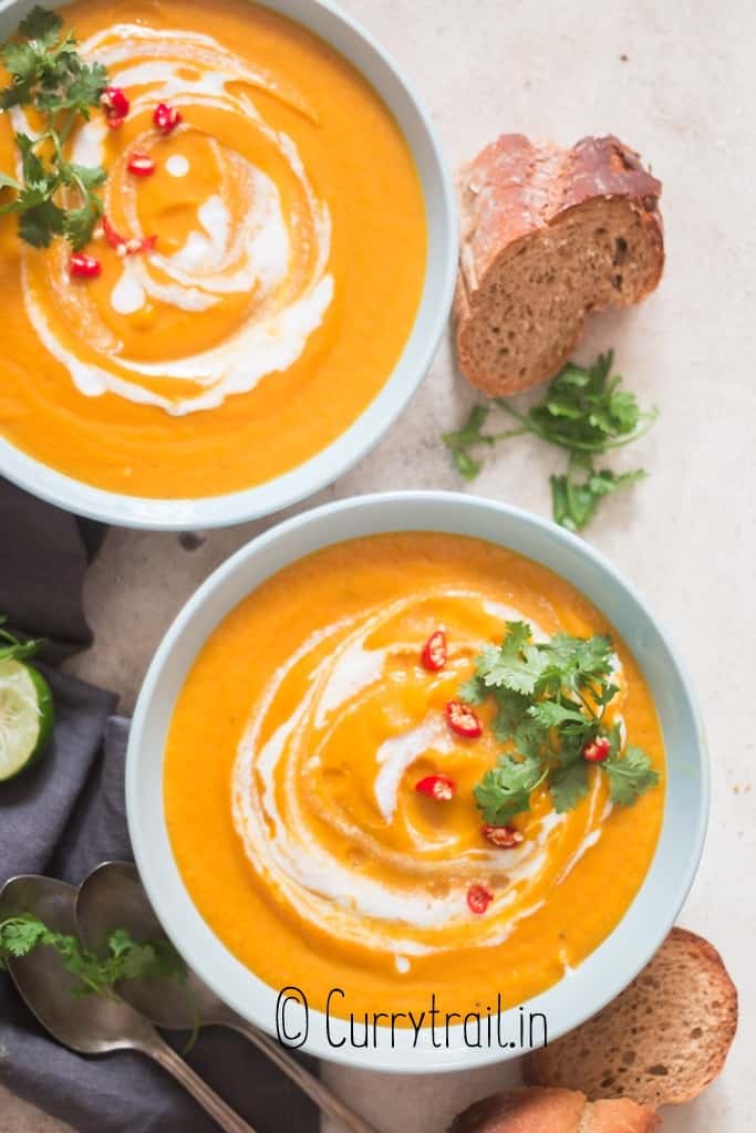 Thai vegan pumpkin curry soup in 2 bowls with crusty bread on sides