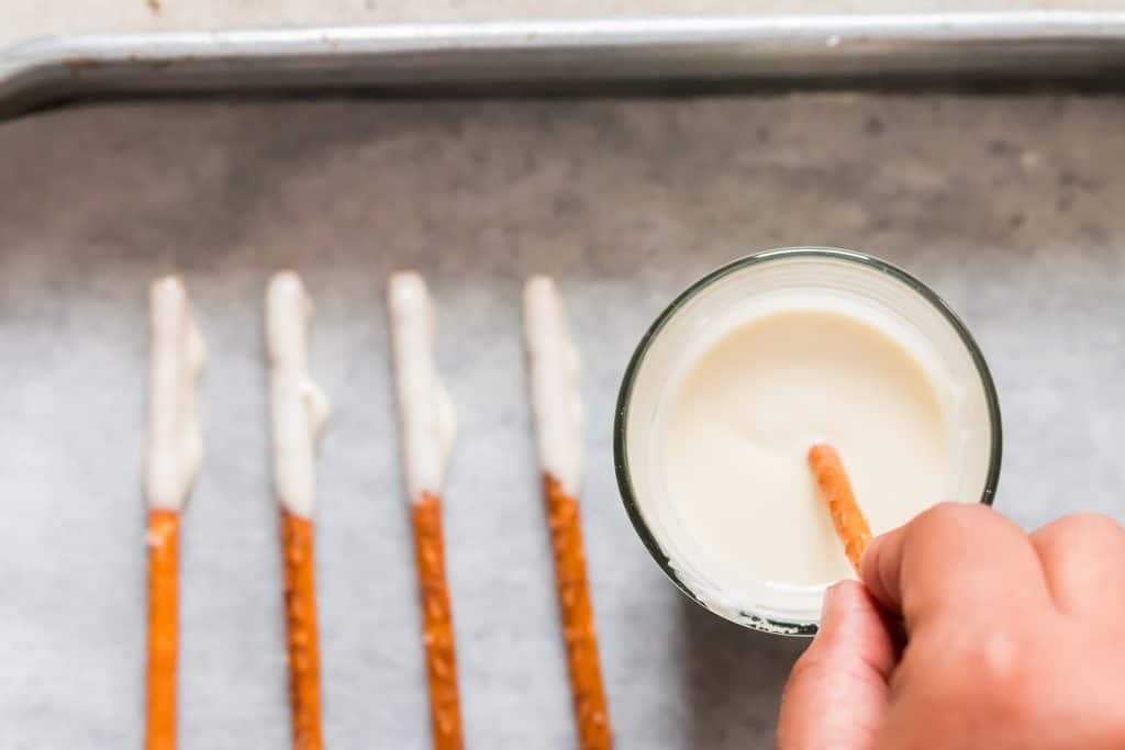 mojar palitos de pretzel en chocolate blanco derretido