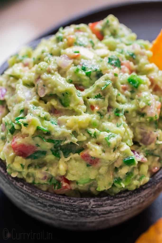 guacamole served in black stone bowl with nachos on sides