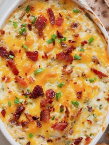 Close-up view of a creamy cheesy dip in a casserole dish with crackers on the side.