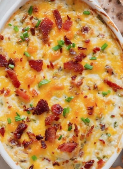 Close-up view of a creamy cheesy dip in a casserole dish with crackers on the side.