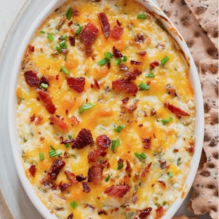 Close-up view of a creamy cheesy dip in a casserole dish with crackers on the side.